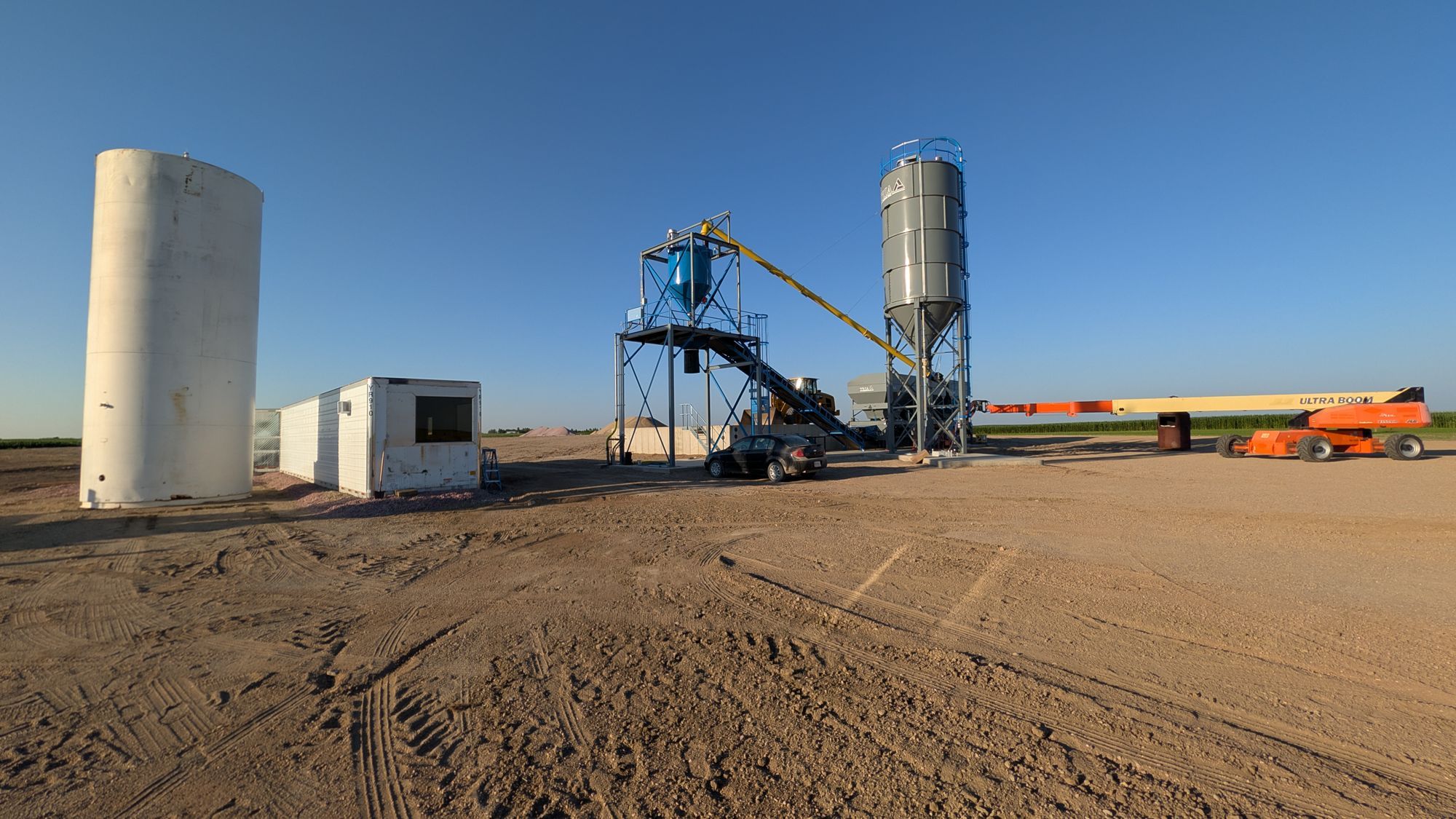 Batch plant silos and aggregate piles, seen from across the yard.